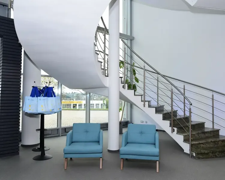 Zwei hellblaue Sessel und ein Stehtisch mit Tragetaschen unter der Wendeltreppe