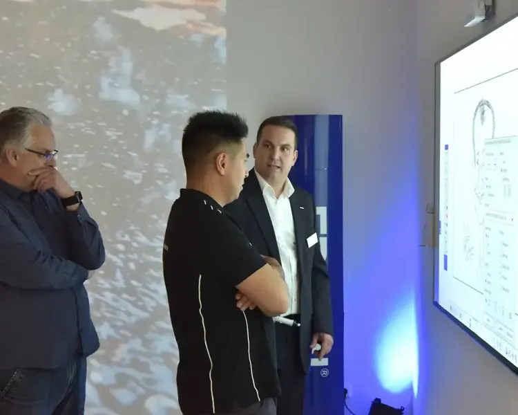 Drei Personen vor einem interaktiven Display mit technischer Zeichnung