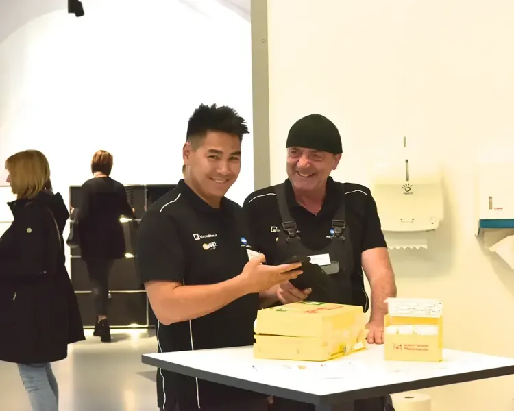 Zwei Mitarbeiter lachen an einem Tisch mit gelben Verbrauchsmaterial-Verpackungen