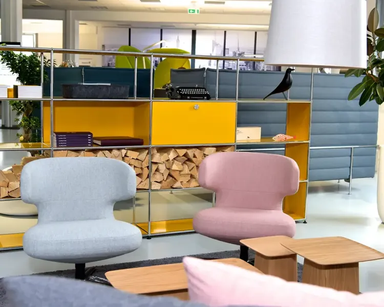 Sessel in Hellblau und Rosa vor einem gelben USM-Haller-Regal mit Brennholz