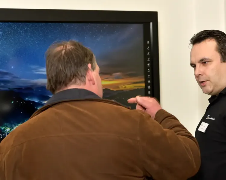 Berater erklärt einem Besucher ein großformatiges Display mit Sternenhimmel