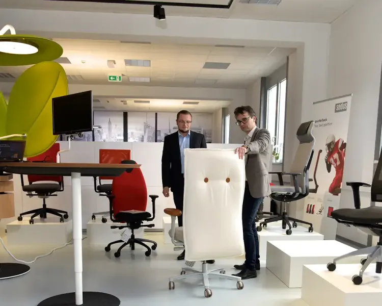 Zwei Berater in der Stuhlausstellung, einer hält eine hohe Rückenlehne