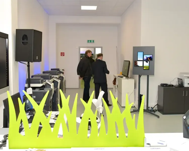 Grüne Grasskulptur als Sichtschutz, dahinter Drucker und Besucher