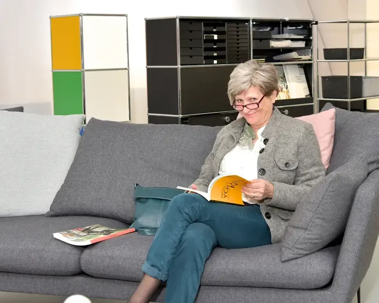 Besucherin liest auf einem grauen Sofa in der Ausstellung