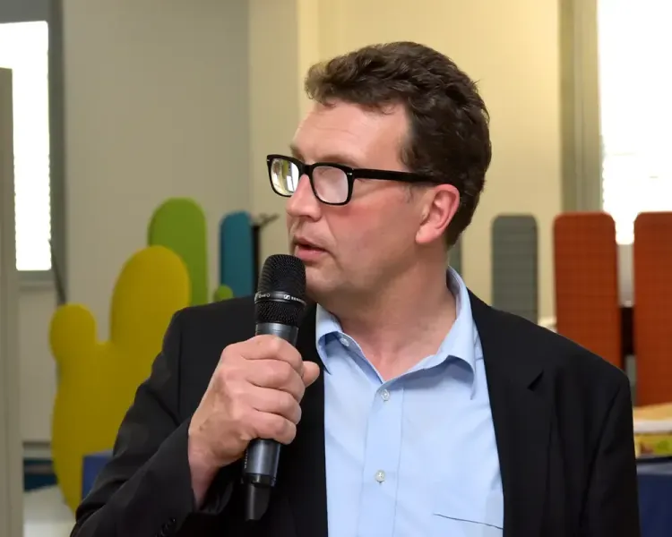 Redner mit Mikrofon vor bunten Akustikelementen