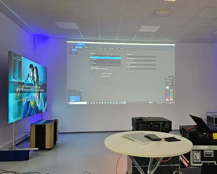 Zwei Projektionsflächen nebeneinander, davor ein Tisch mit Notebook und Projektortechnik