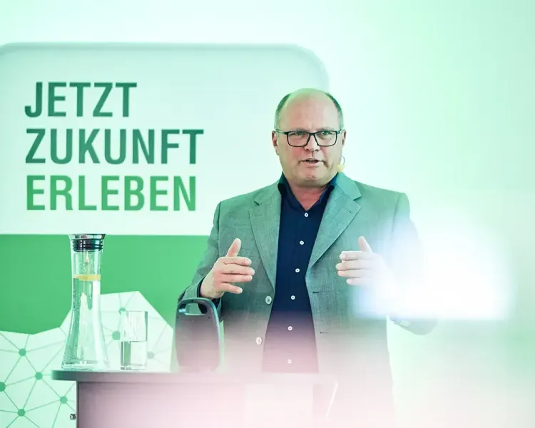 Redner am Pult vor der Wand „Jetzt Zukunft erleben“
