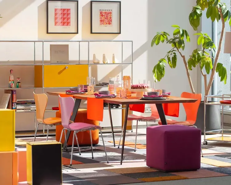Besprechungstisch mit farbigen Stühlen in Orange und Violett vor einem Regalsystem