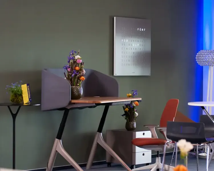 Einzelarbeitsplatz mit Sichtschutz und Blumenschmuck vor olivgrüner Wand