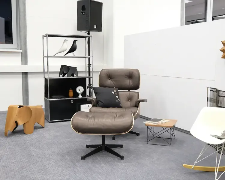 Lounge-Sessel mit Fußhocker neben einem schwarzen Regal mit Designobjekten