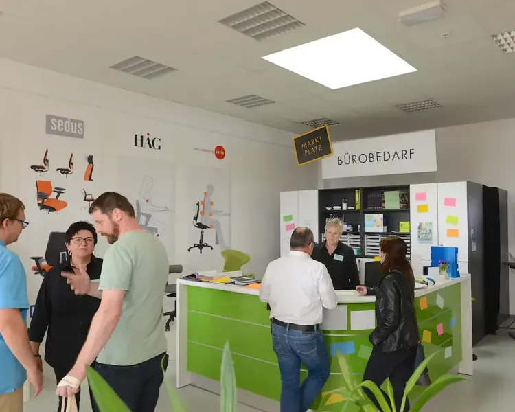 Besucher am Tresen des Bereichs „Bürobedarf“ vor der Herstellerwand