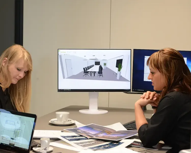Zwei Planerinnen am Besprechungstisch, auf dem Bildschirm eine 3D-Raumplanung