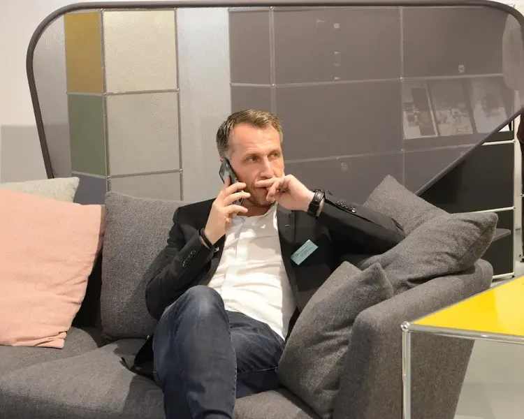 Besucher telefoniert in einer Sofanische vor einer Wand mit Stoffmustern