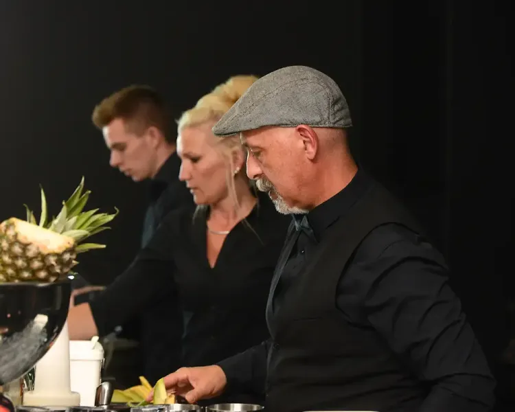 Drei Personen in schwarzer Kleidung bereiten am Buffet Speisen zu