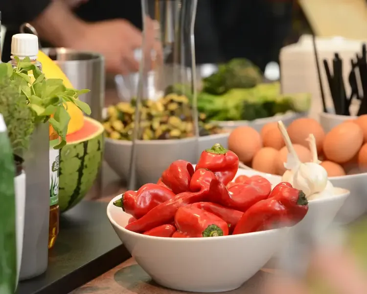 Schale mit roten Spitzpaprika, dahinter Eier, Brokkoli und Melone am Buffet