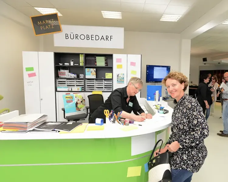 Besucherin am Tresen des Bereichs „Bürobedarf“, dahinter eine Mitarbeiterin