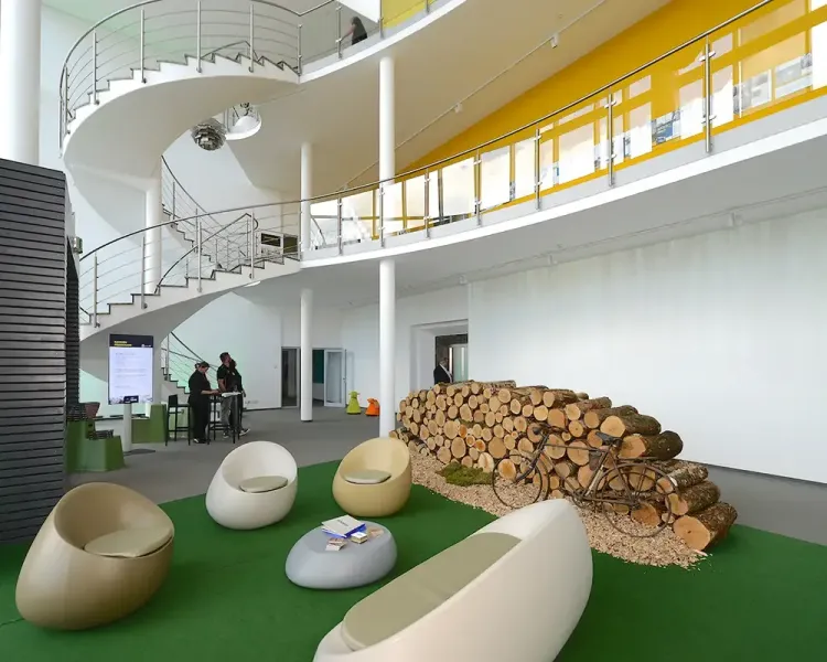 Foyer mit Wendeltreppe, Sitzeiern auf Kunstrasen und einem Holzstapel
