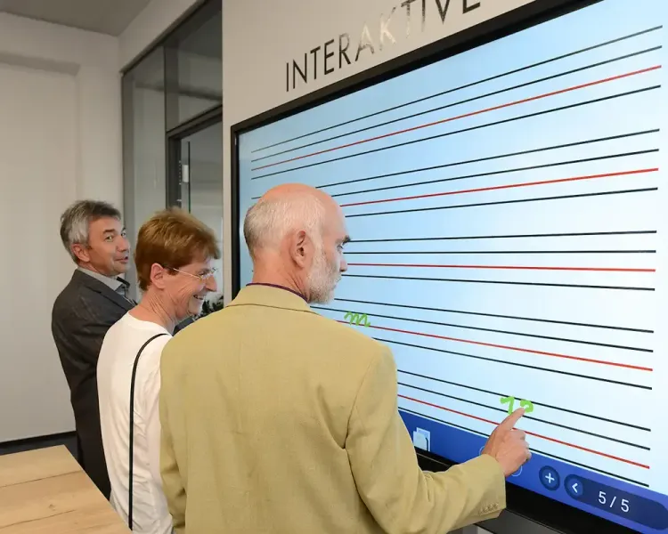 Drei Besucher bedienen ein interaktives Großdisplay