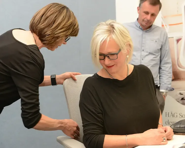 Beraterin stellt einer sitzenden Besucherin die Rückenlehne eines Bürostuhls ein