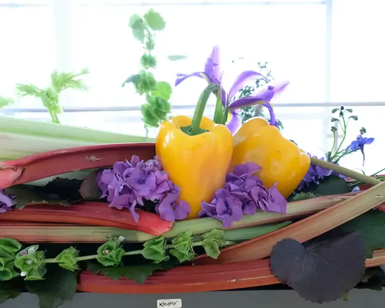 Gesteck aus gelben Paprika, Hortensien und Rhabarberstangen vor der Fensterfront