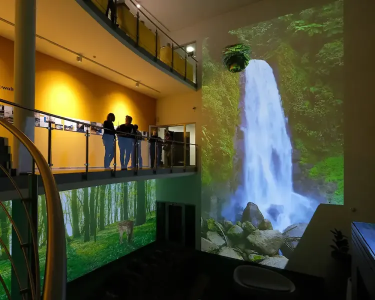 Zweigeschossiges Foyer mit Wasserfall- und Waldprojektion, Besucher auf der Galerie
