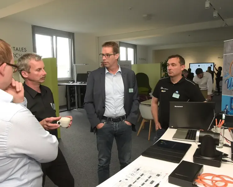 Vier Besucher im Gespräch an einem Technik-Arbeitsplatz