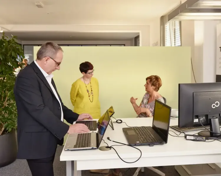 Drei Personen an einem Steh-Sitz-Tisch mit zwei Notebooks