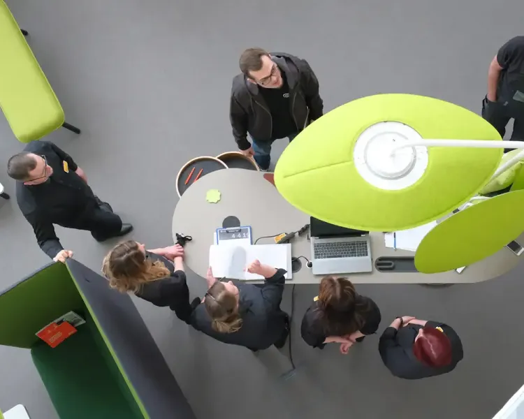 Blick von oben auf eine Besuchergruppe an einem Stehtisch mit Akustikleuchte