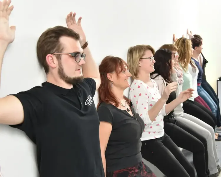 Teilnehmende machen eine Rückenübung an der Wand