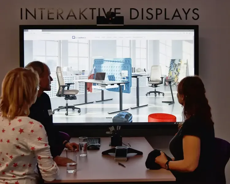 Drei Personen an einem Konferenztisch vor der Wand „Interaktive Displays“