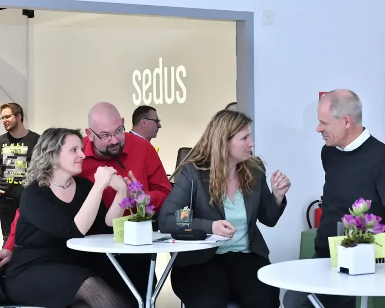 Gäste an zwei Stehtischen im Gespräch, an der Wand der Schriftzug „sedus“