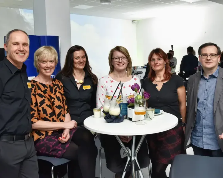 Sechs Gäste an einem Tisch mit Cocktails, im Hintergrund eine Himmelsprojektion