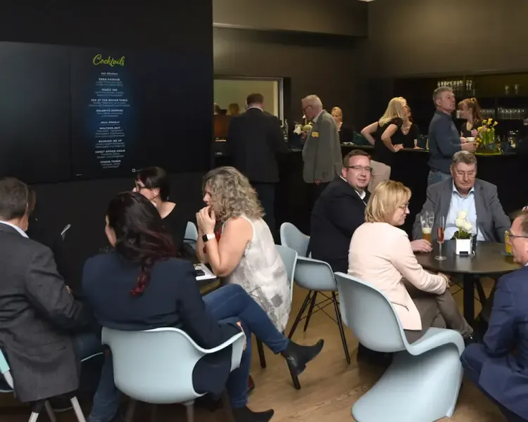 Gäste an Tischen in der Cocktailbar, links die beleuchtete Getränkekarte