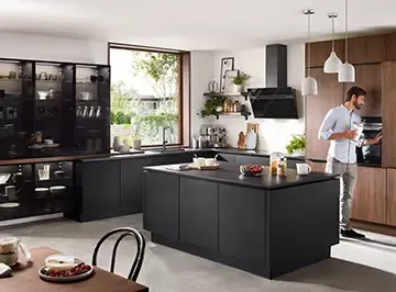Schwarze Küche mit Kochinsel und Holzelementen, ein Mann räumt den Backofen ein